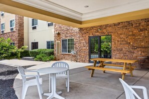 An outdoor patio with a stone wall, a wooden picnic table, and white plastic chairs. - Comfort Suites Grayslake near Libertyville North (Grayslake)