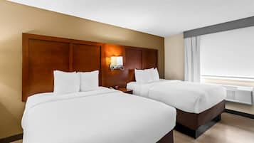 Habitación de hotel con dos camas, cabecera de madera, mesita de noche, lámpara y un ventanal grande.