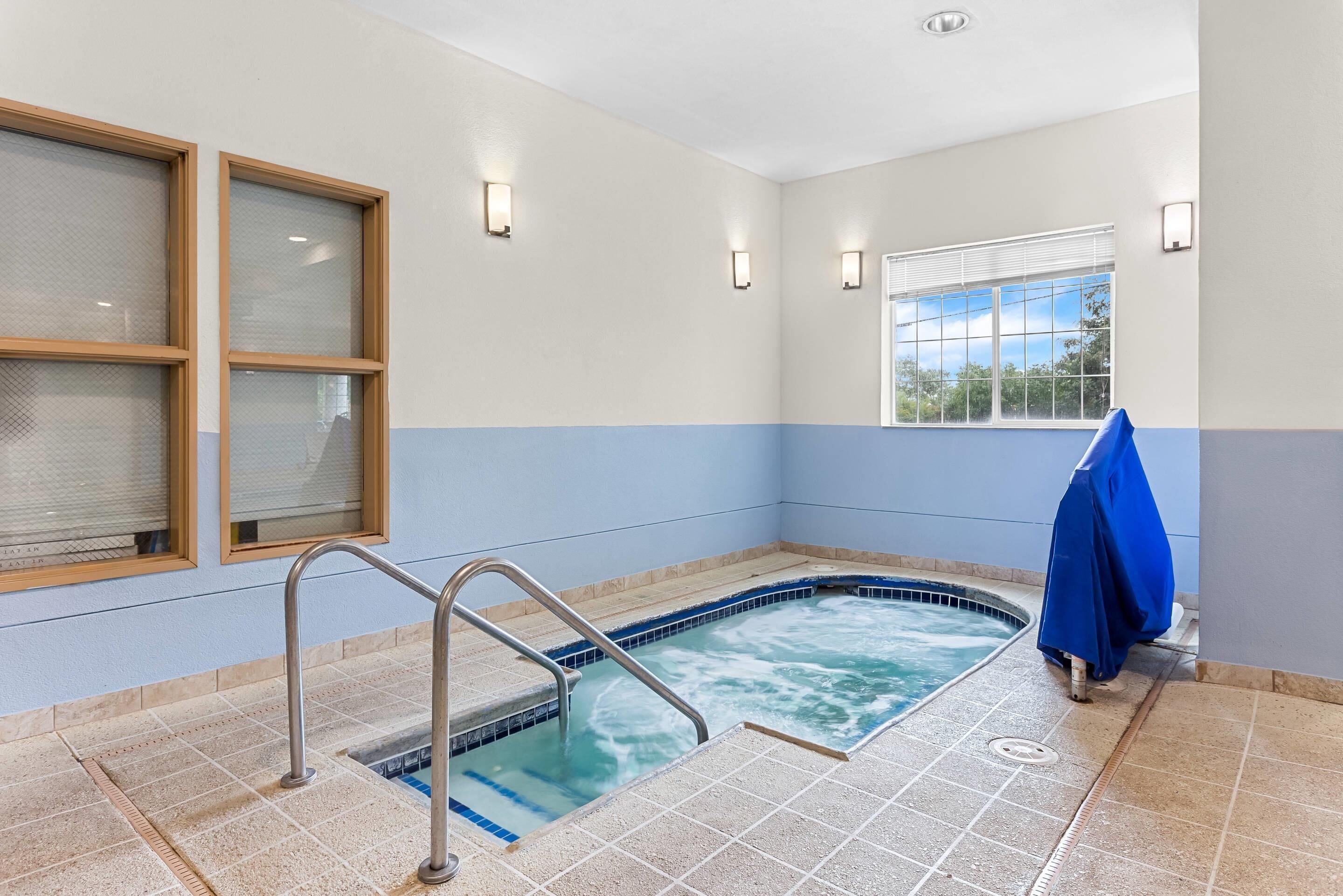 A spa area with a hot tub, a window with blinds, and a blue towel on a rack.