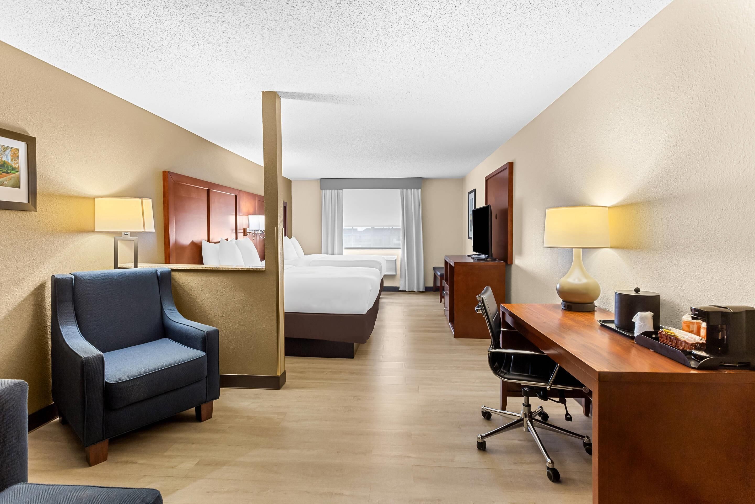 A hotel room with a bed, a desk with a lamp, a chair, and a desk lamp.