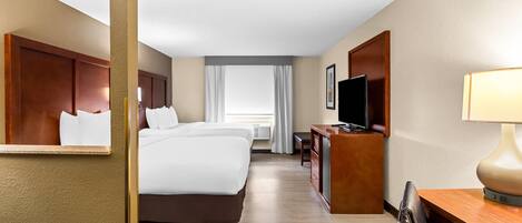 A hotel room with a large bed, a desk, a TV, and a lamp.