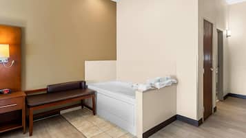 Una habitación de hotel con cama, un banco, una mesita y la puerta del baño.