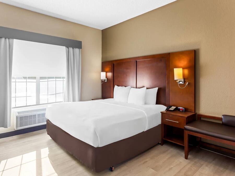 A hotel room with a large bed, bedside lamps, a bedside table, a sofa, and a window with curtains.
