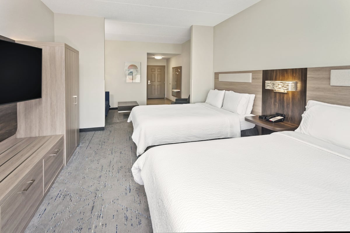 A hotel room with two beds, a TV, a desk with a phone, and a wall-mounted light fixture.