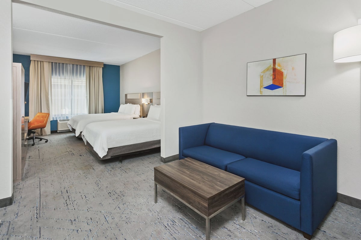 A hotel room with a bed, a blue sofa, a wooden coffee table, and a chair.