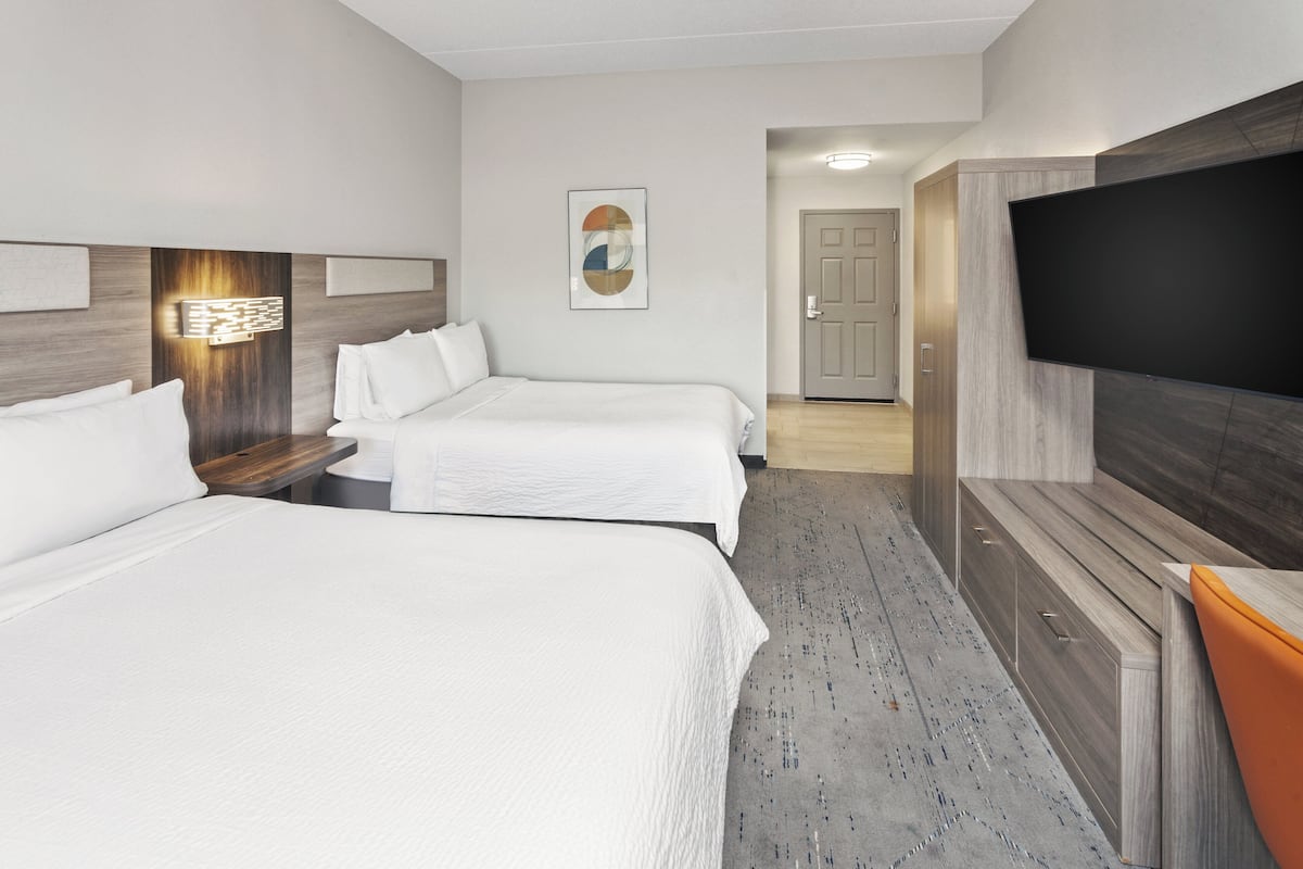 A hotel room with two beds, a flat-screen TV, a wooden cabinet, and a painting on the wall.