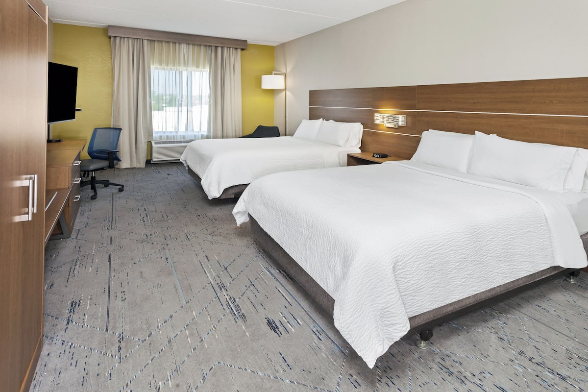A hotel room with two beds, a desk, a chair, a TV, and a window with curtains.