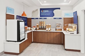 Un comedor con refrigerador, cafetera y una selección de frutas, cereales y productos de panadería.