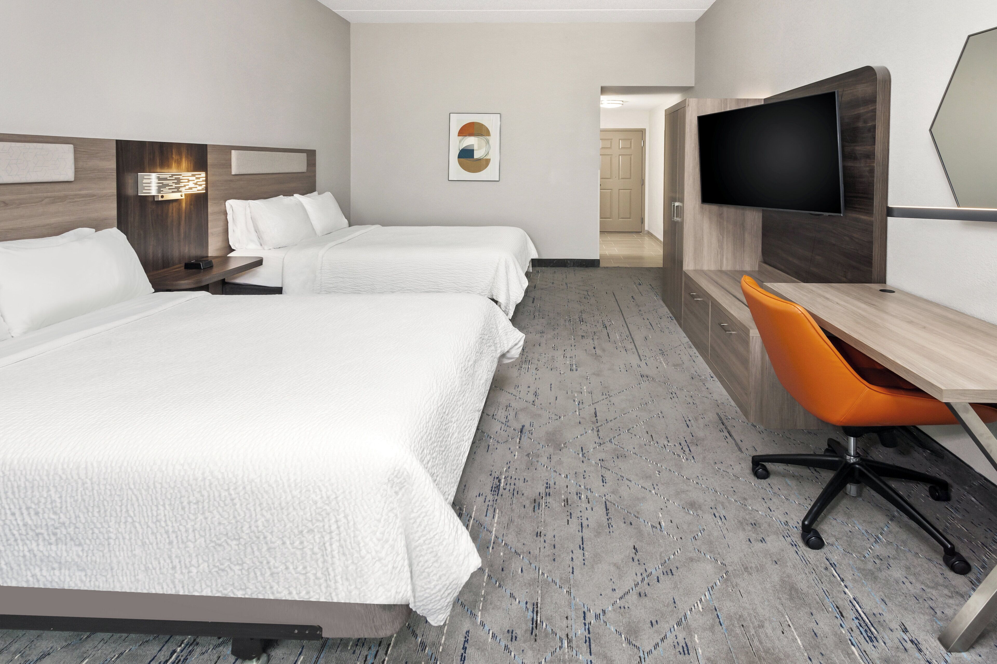 A hotel room with two beds, a desk with an orange chair, a flat-screen TV, and a wall-mounted artwork.