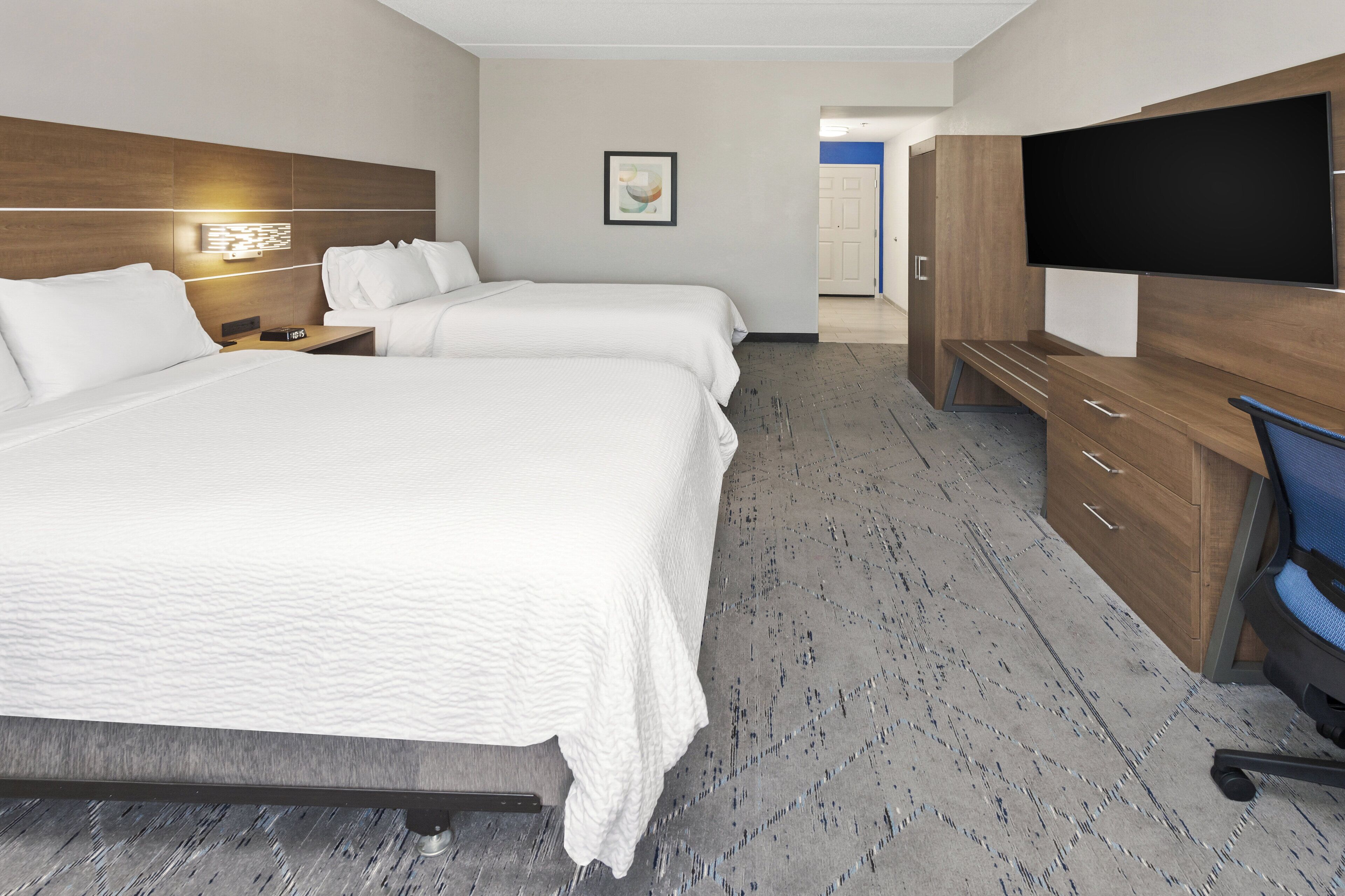 A hotel room with two beds, a desk, a flat-screen TV, and a wooden wardrobe.
