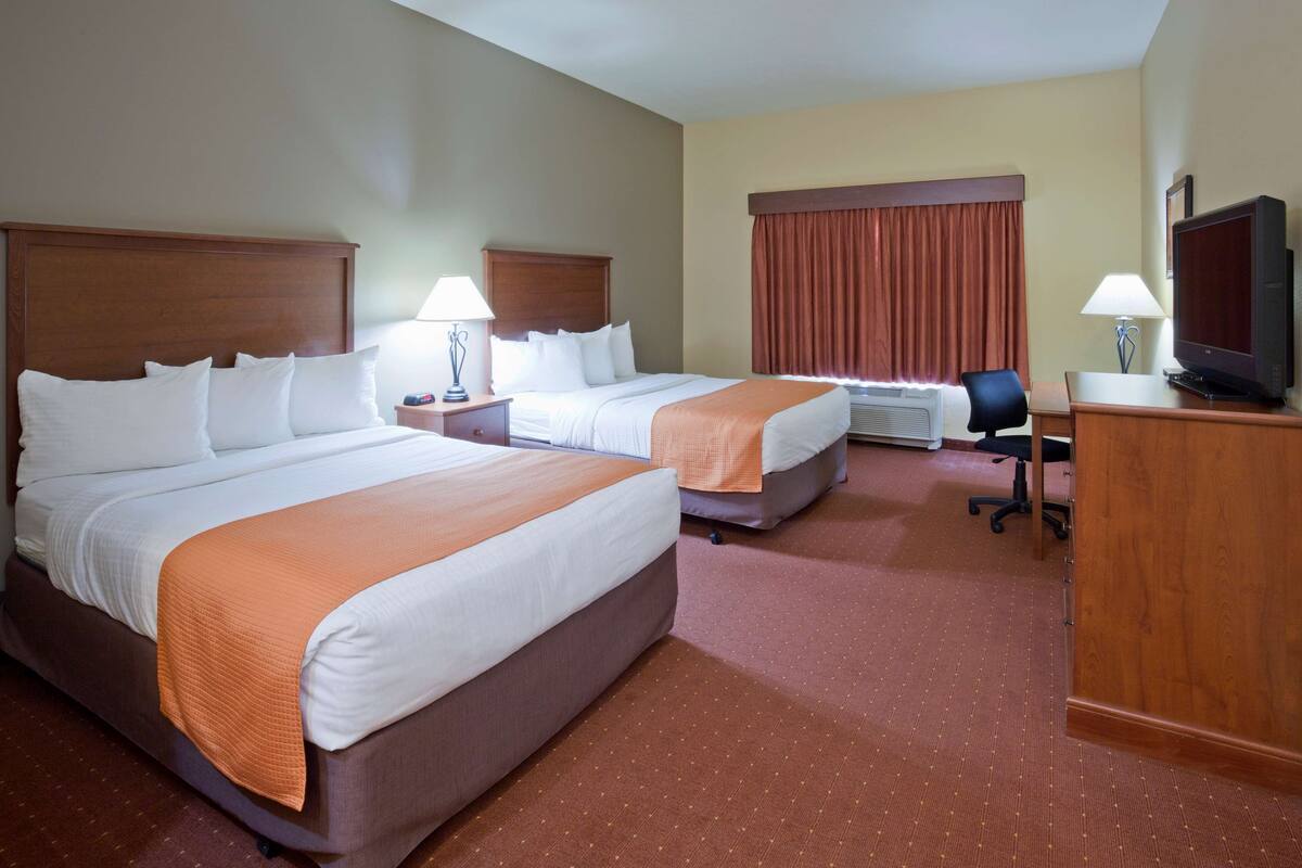 A hotel room with two beds, a desk with a television, and a chair.