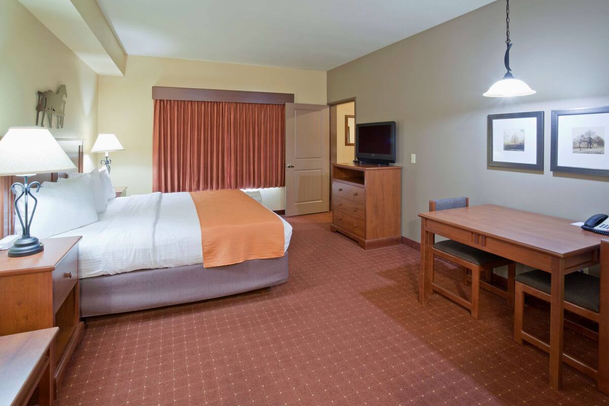 A hotel room with a bed, bedside table, lamp, desk, chair, television, and framed pictures on the wall.