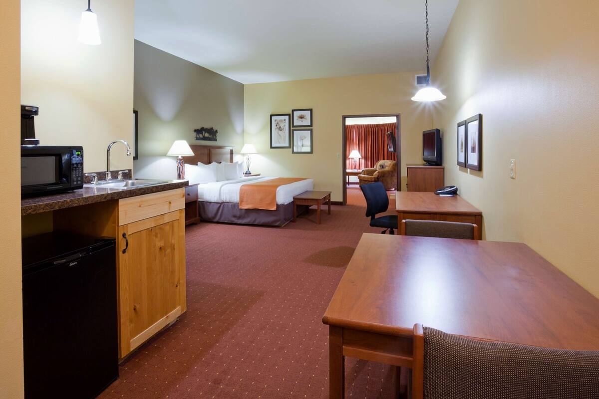 A compact hotel room with a kitchenette, a bed, a dining table, and a chair.