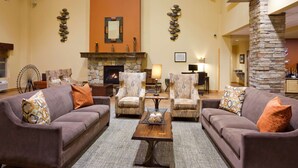 Un salon spacieux avec une cheminée en pierre, deux canapés, une table basse et des fauteuils à motifs.