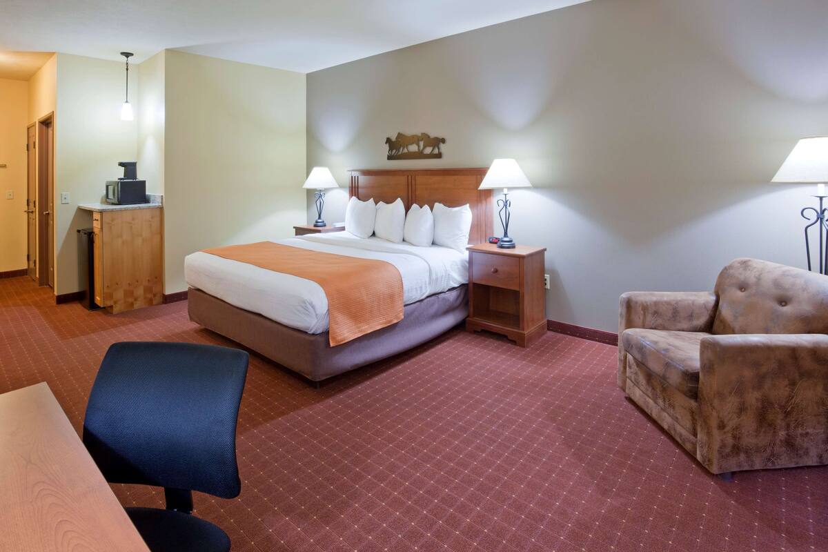 A hotel room with a bed, two bedside tables with lamps, a chair, a desk, and a small cabinet.