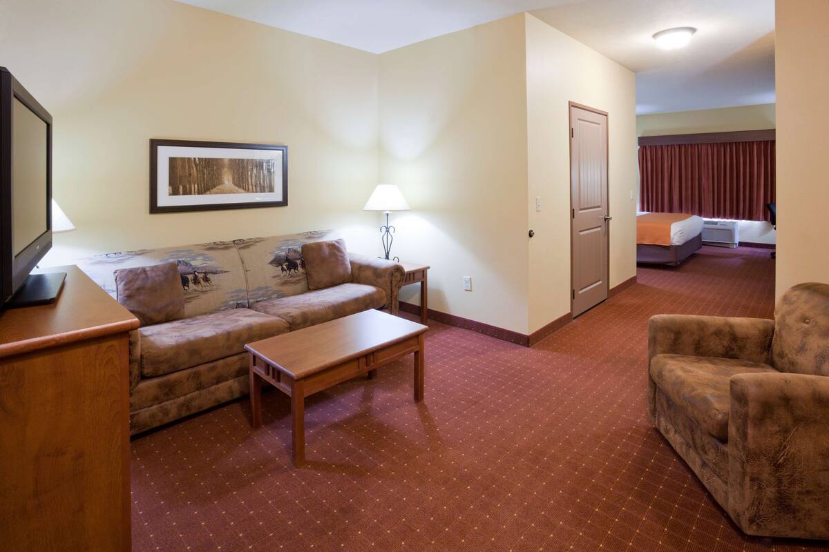 A hotel room with a sofa, a small table, a lamp, a television, and a door leading to another room.