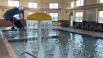 Una piscina interior con tobogán de agua, un puesto de socorrista y una zona de estar con sillas.