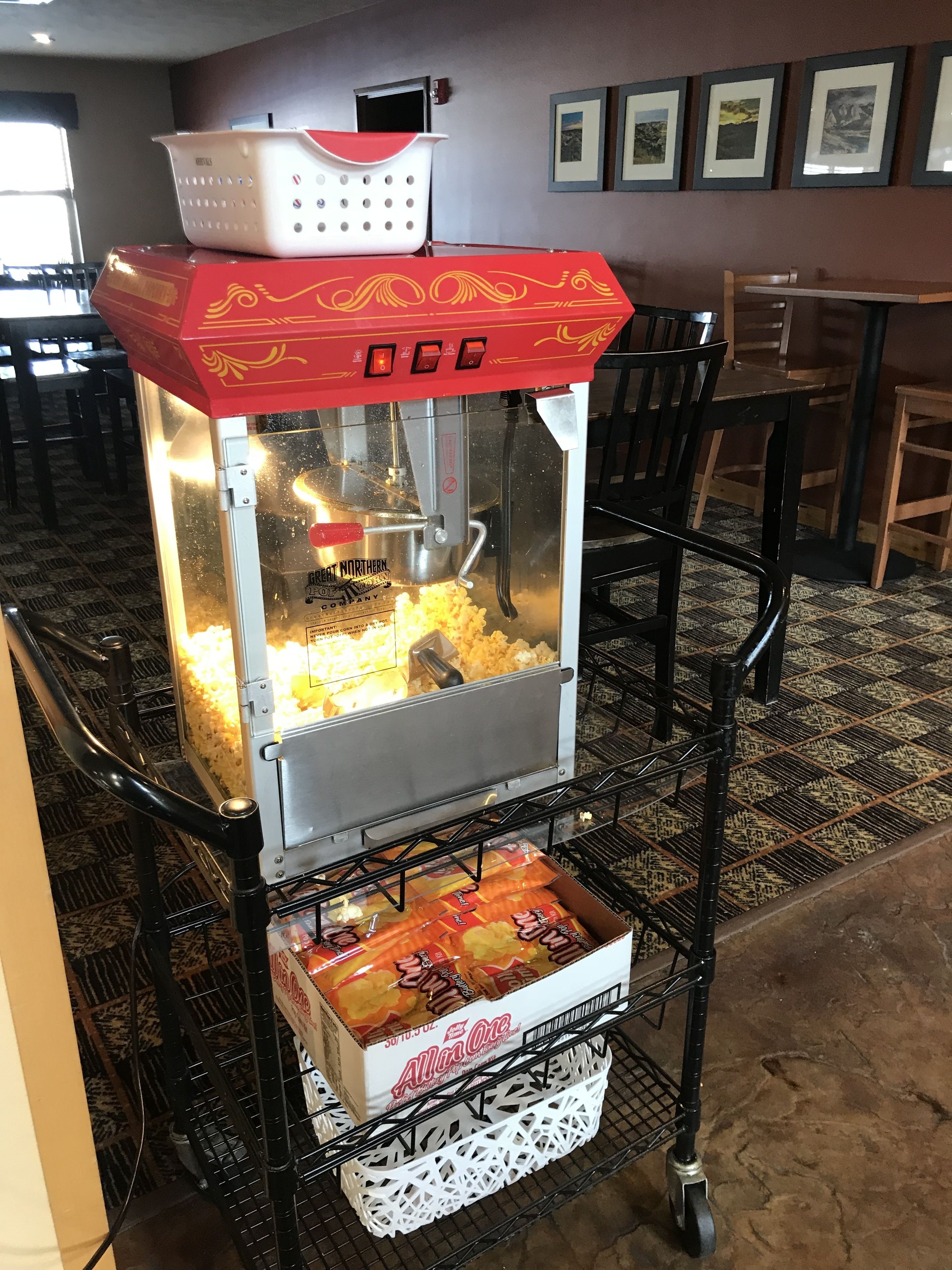 A popcorn machine with a red top and a white basket on top, placed on a metal cart.