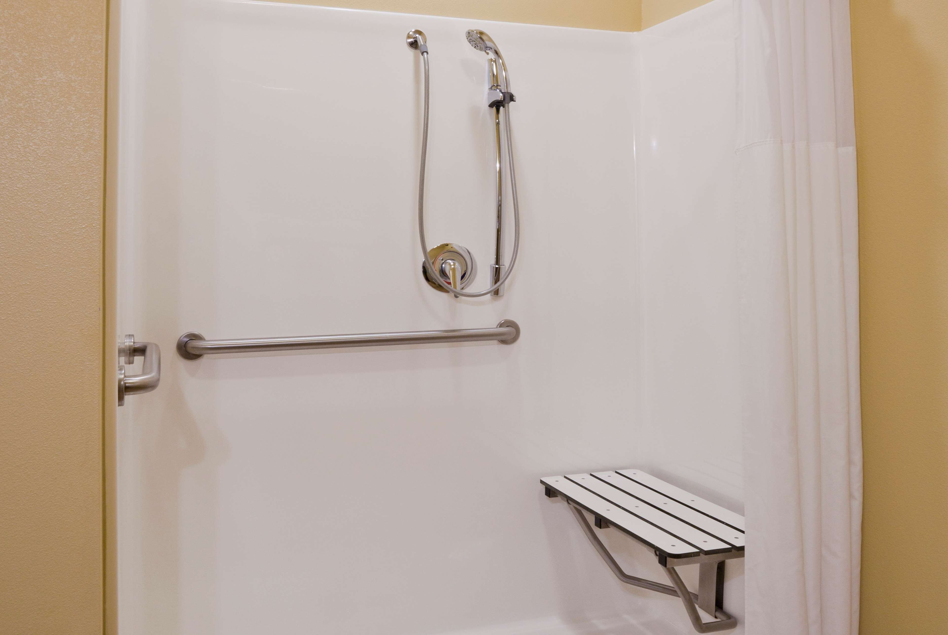 A white shower enclosure with a handheld showerhead and a handheld shower attachment.