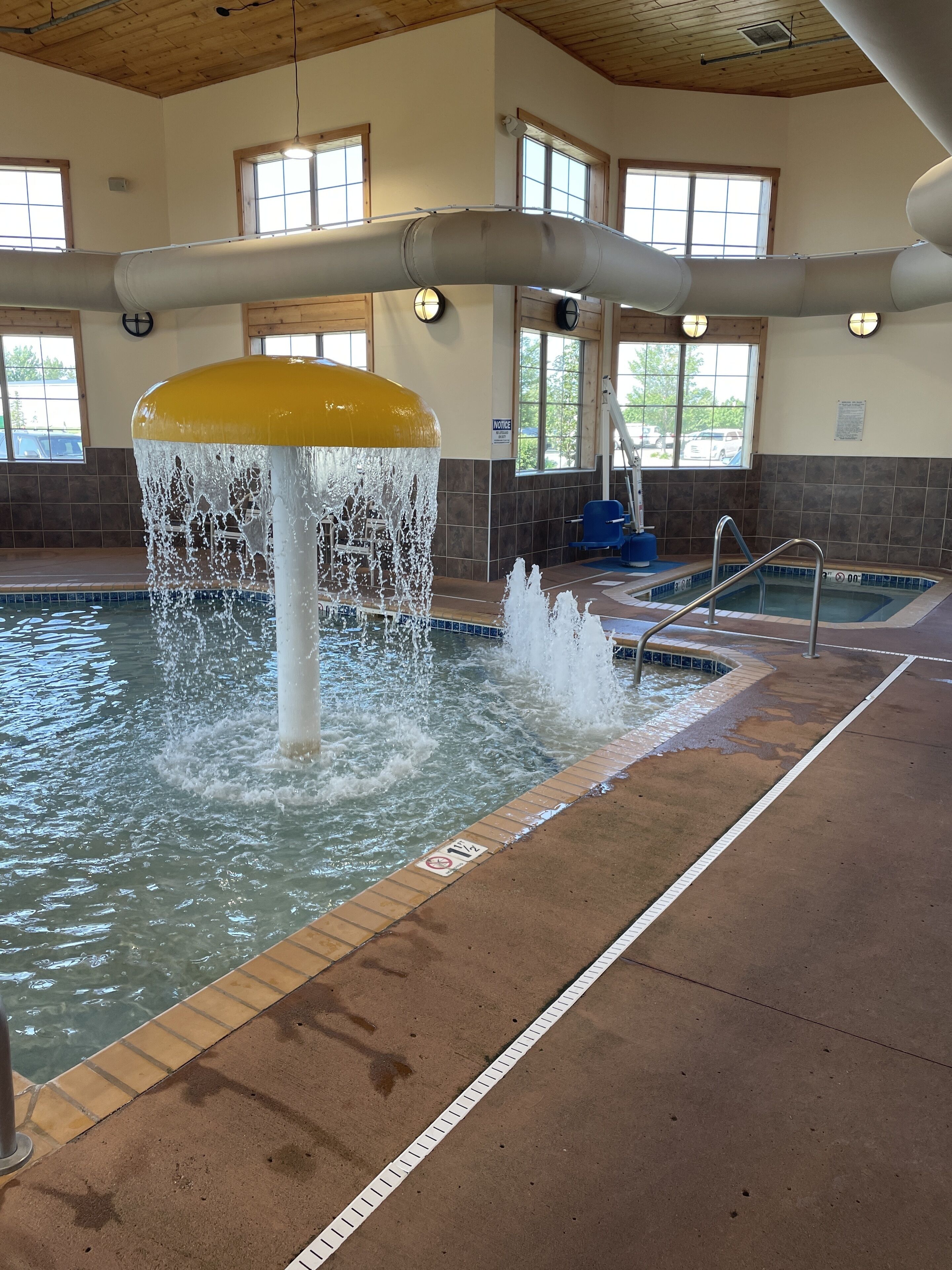 An indoor swimming pool with a central water feature, clear poolside area, and natural light from windows.