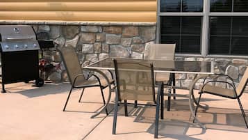 An outdoor patio with a grill, chairs, and a table.