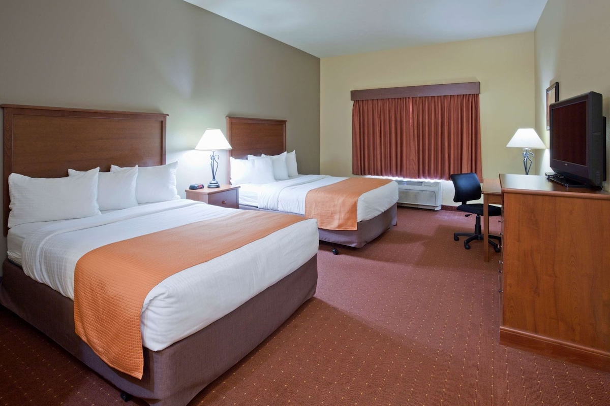 A hotel room with two beds, a desk, a television, and a window with curtains.
