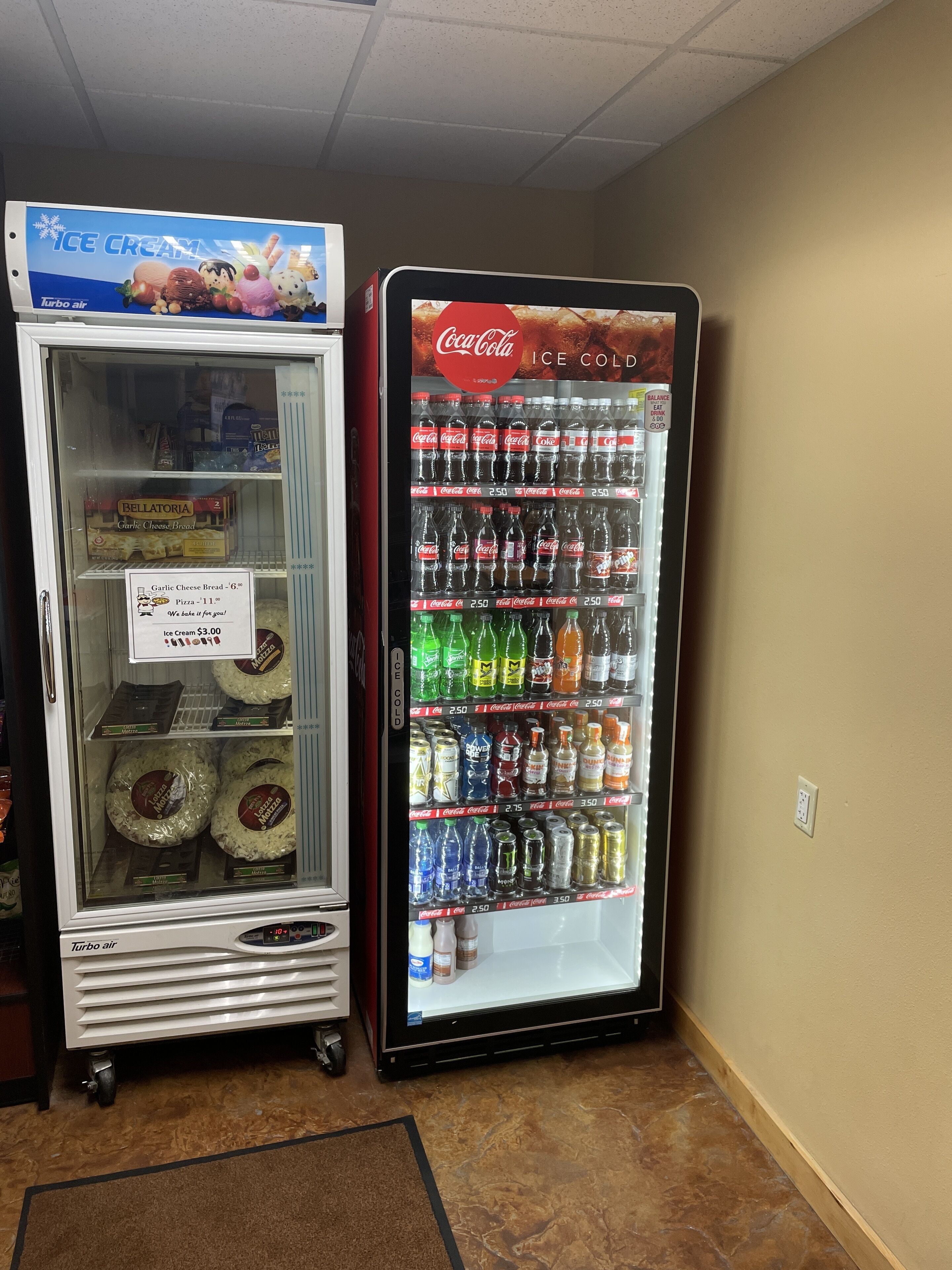 Twee drankautomaten, waarvan één ijs verkoopt en de andere Coca-Cola en andere frisdranken.