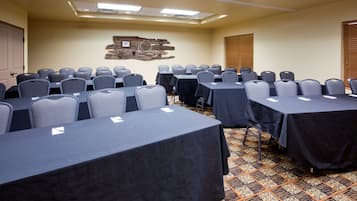 Un salón de conferencias con varias mesas y sillas, una alfombra estampada y una obra de arte colgada en la pared.