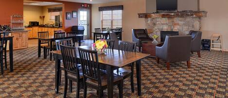 A dining area with a large wooden table and chairs, a stone fireplace, and a television mounted above it.