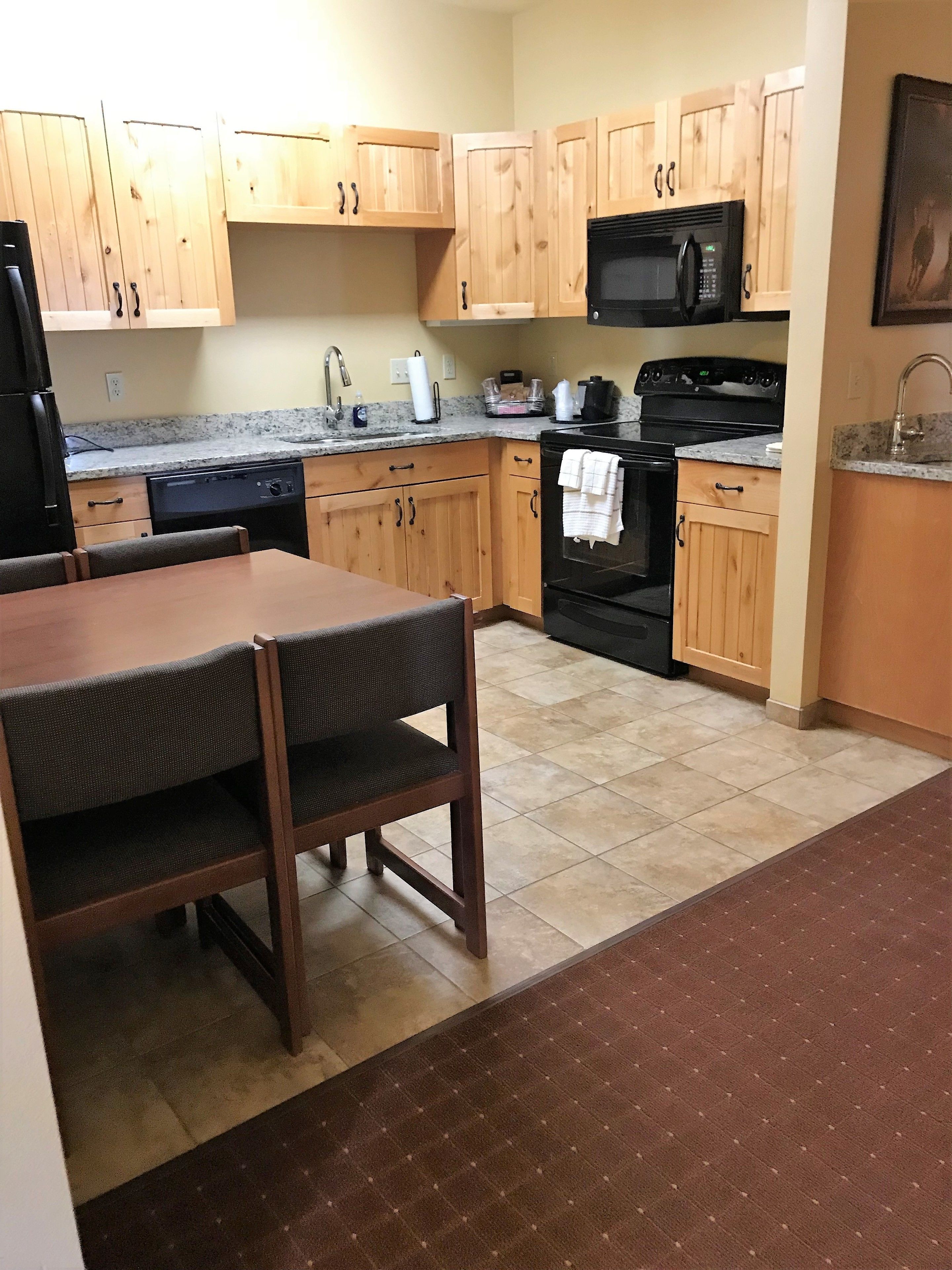 A kitchen with wooden cabinets, a black microwave, a stove, and a dining area with a table and chairs.