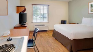Habitación de hotel con cama, escritorio con televisor, silla, ventana con persianas y unidad de aire acondicionado.