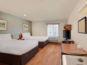 A hotel room with two beds, a television, a desk with a telephone, and a window with blinds.