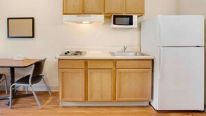 Una cocina compacta con armarios de madera, un refrigerador blanco, un microondas y un lavamanos.