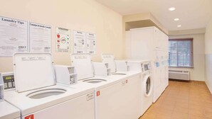 Un cuarto de lavandería con cuatro lavadoras y cuatro secadoras, numeradas del 1 al 4, y una pared con consejos para el lavado e instrucciones del servicio.