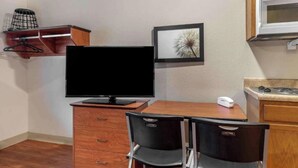 A small kitchenette with a microwave, a stove, and a sink. There is a TV on a wooden stand, a framed picture on the wall, and two chairs. - Studio 6 Extended Stay Shreveport Airport LA (Shreveport)