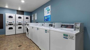 Une buanderie équipée de plusieurs machines à laver et de plusieurs sèche-linge, d’un panneau de commande et d’une affiche accrochée au mur.