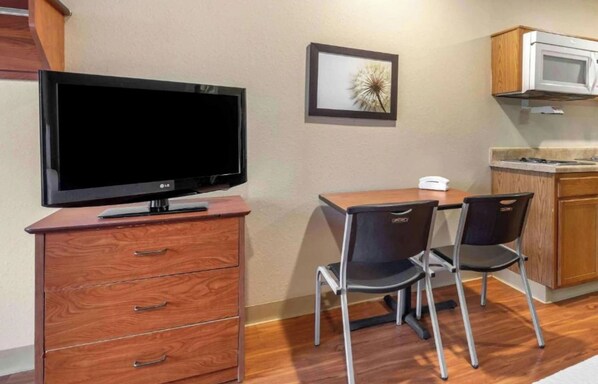 A kitchenette with a microwave, a small table with two chairs, a TV on a wooden cabinet, and a framed picture on the wall.