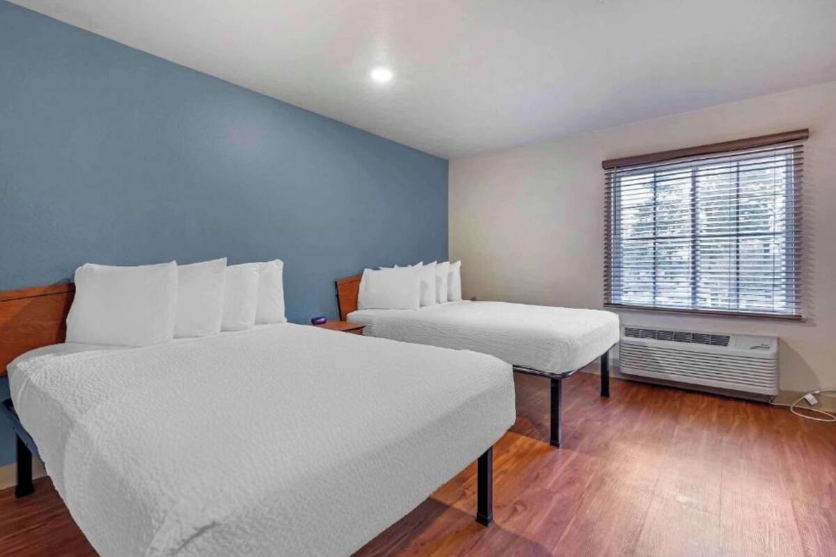 A room with two beds, a window with blinds, and a wall heater.