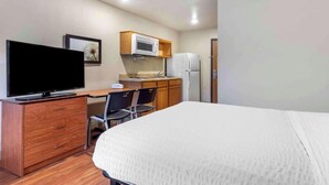 A hotel room with a bed, a TV on a wooden dresser, a kitchenette with a microwave and refrigerator, and a chair. - Studio 6 Extended Stay Shreveport Airport LA (Shreveport)