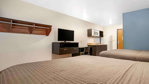 Een hotelkamer met twee bedden, een bureau met een televisie, een magnetron en een klein kitchenette.