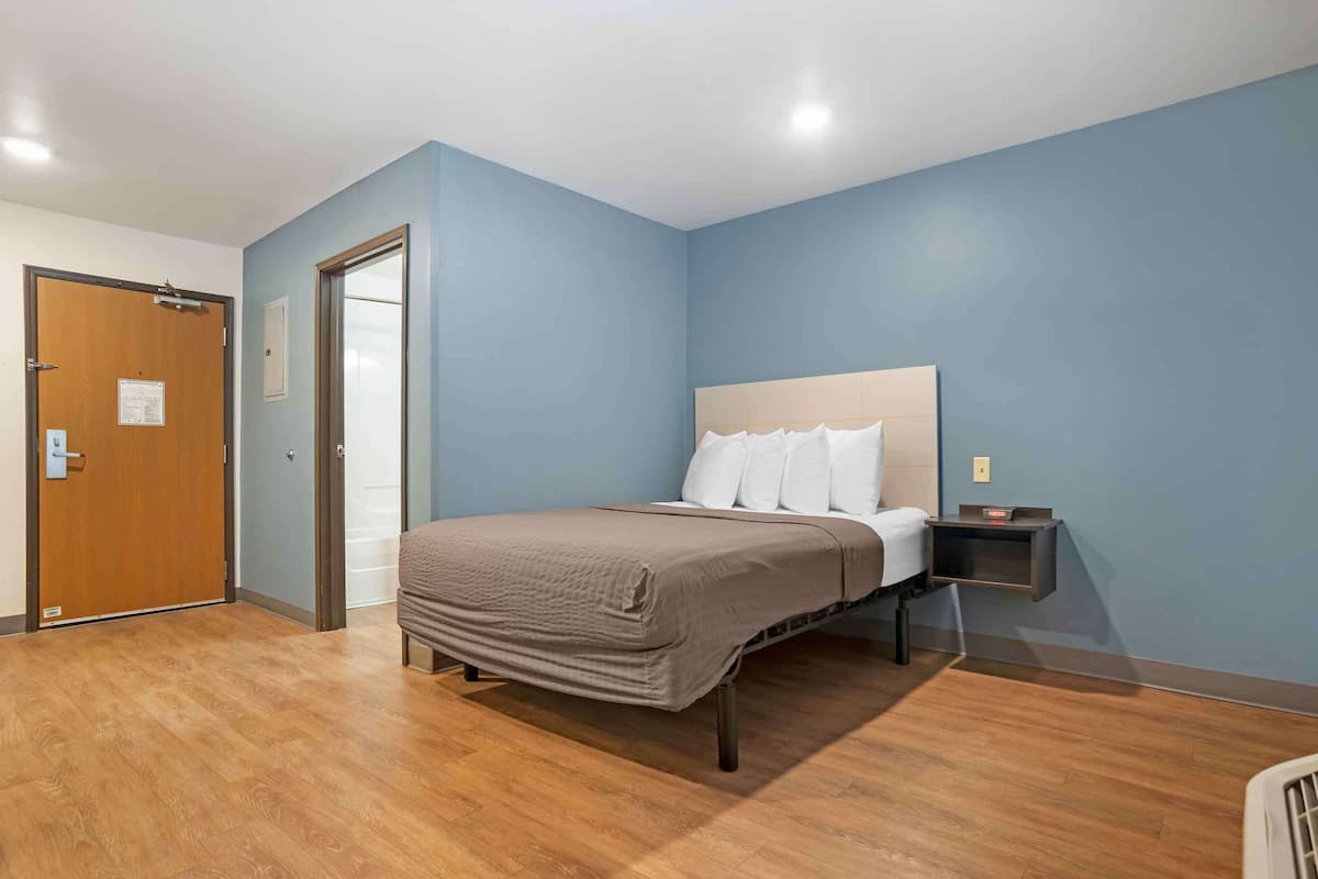 A bedroom with a bed, wooden flooring, a nightstand, and a door.