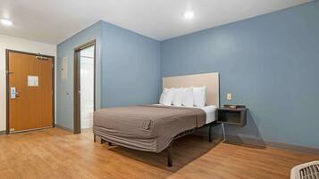 Un dormitorio con cama, suelo de madera, una mesita de noche y una puerta.