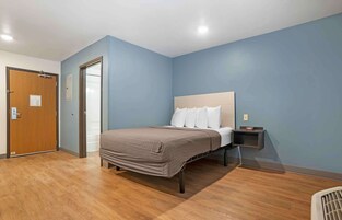 Un dormitorio con cama, suelo de madera, una mesita de noche y una puerta.