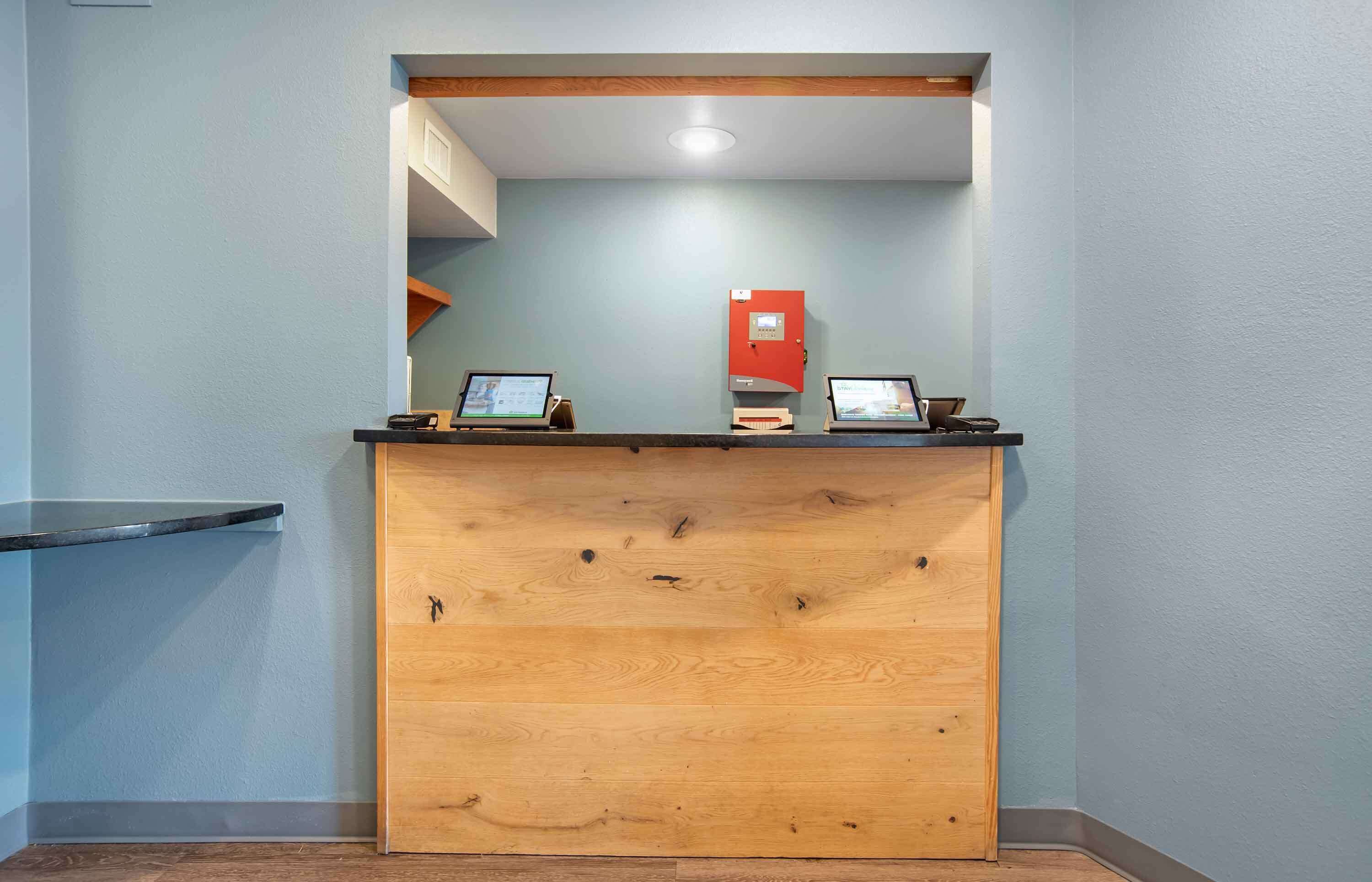 Un comptoir d’accueil avec deux ordinateurs portables, une boîte rouge contenant du matériel de premiers secours et un panneau décoratif en bois.