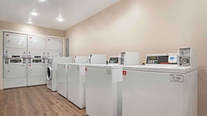 Een wasserette met meerdere wasmachines en drogers, een bedieningspaneel en een digitaal scherm.