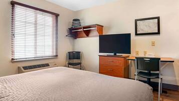 A hotel room with a bed, a desk with a chair, a television, a heater, and a window with blinds.