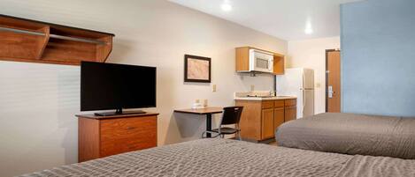 A hotel room with a bed, a desk with a chair, a television, a microwave, and a refrigerator.