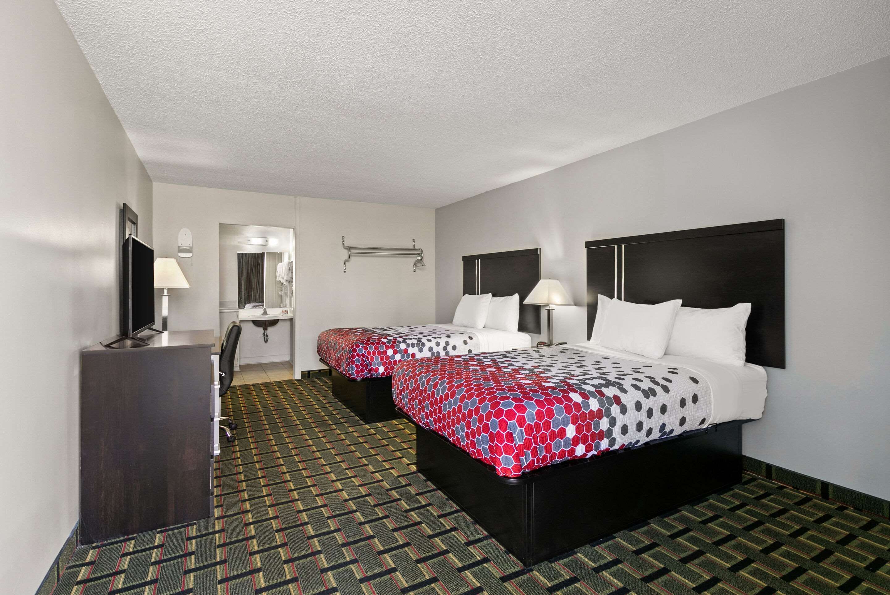 A hotel room with two beds, a desk, a mirror, and a bathroom.