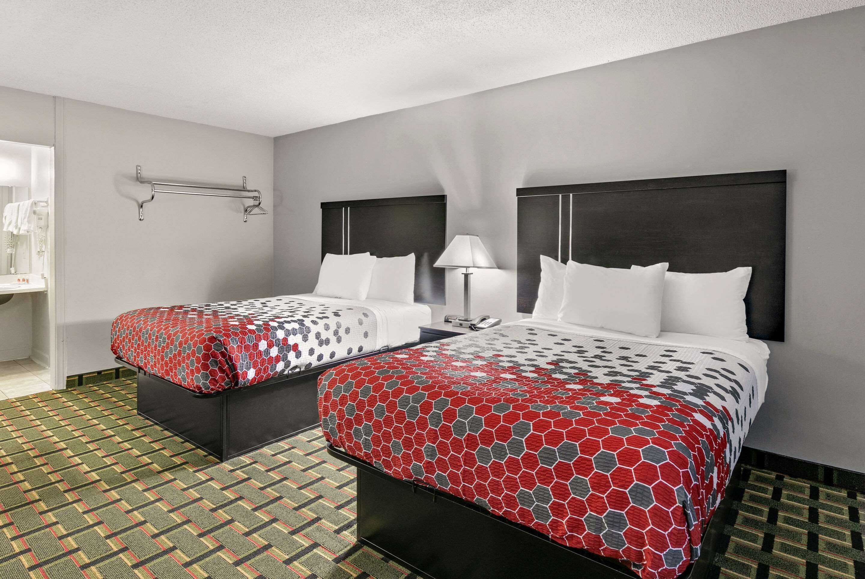 Two beds with dark headboards, a bedside table with a lamp, and a patterned floor.