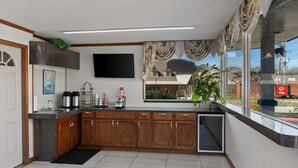 A modern kitchen with wooden cabinets, a built-in dishwasher, a large window with a view of the outside, and a flat-screen TV mounted on the wall. - Econo Lodge Clemson - University Area (Clemson)